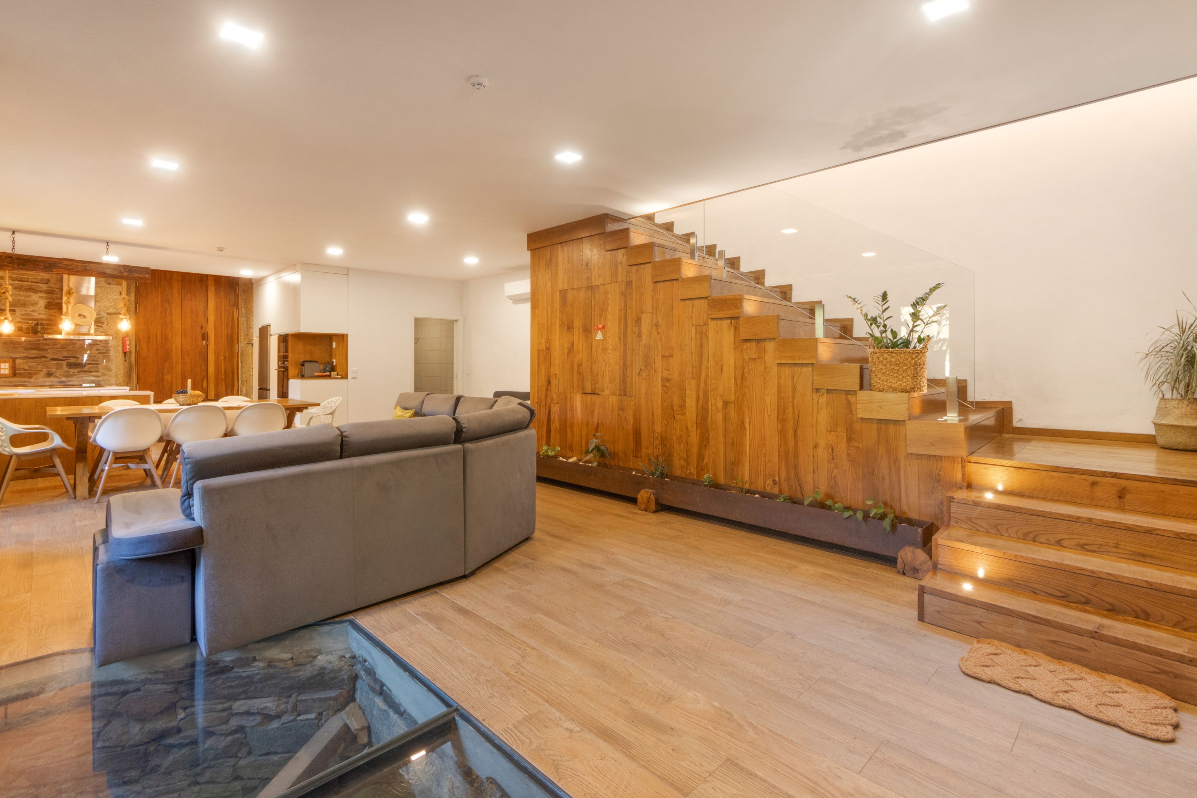 Ein modernes Interieur mit einer Holztreppe, einem grauen Sofa und einem Essbereich mit weißen Stühlen.
