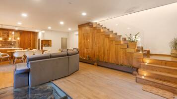 Ein modernes Interieur mit einer Holztreppe, einem grauen Sofa und einem Essbereich mit weißen Stühlen.