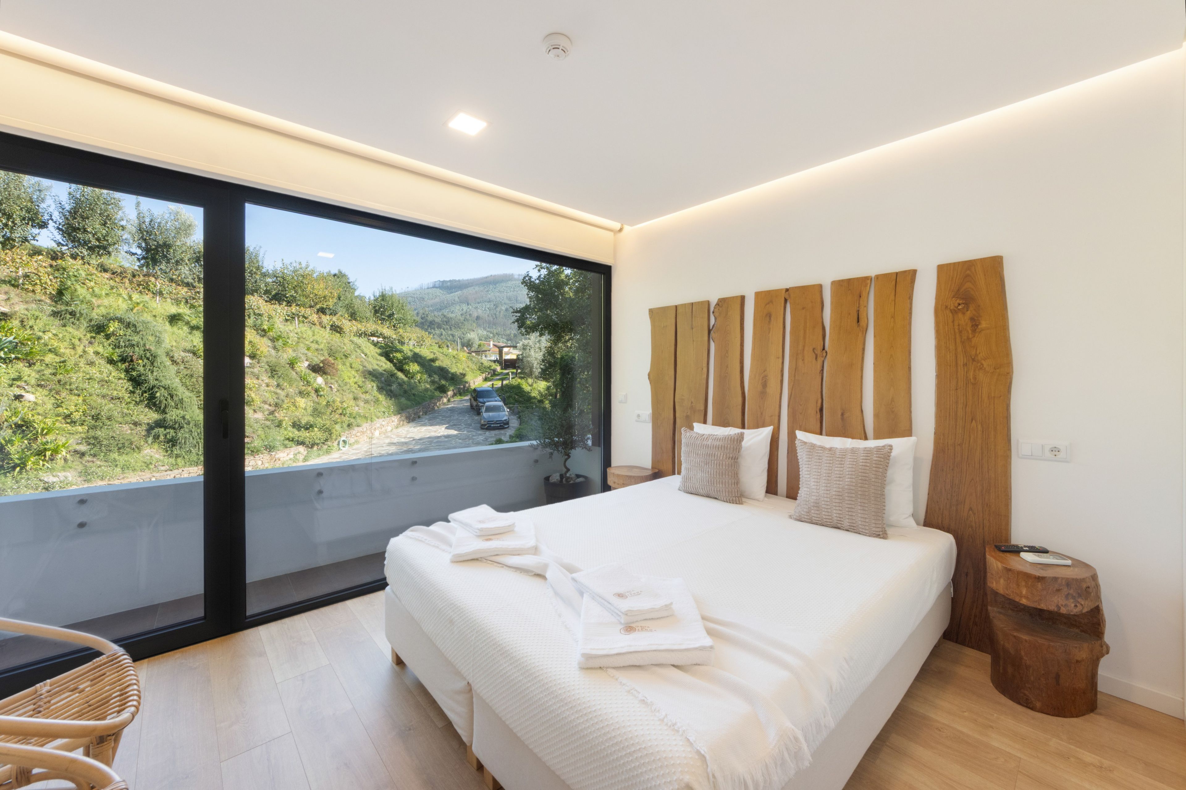 A modern bedroom with a large bed, a wooden headboard, and a view of a hillside.