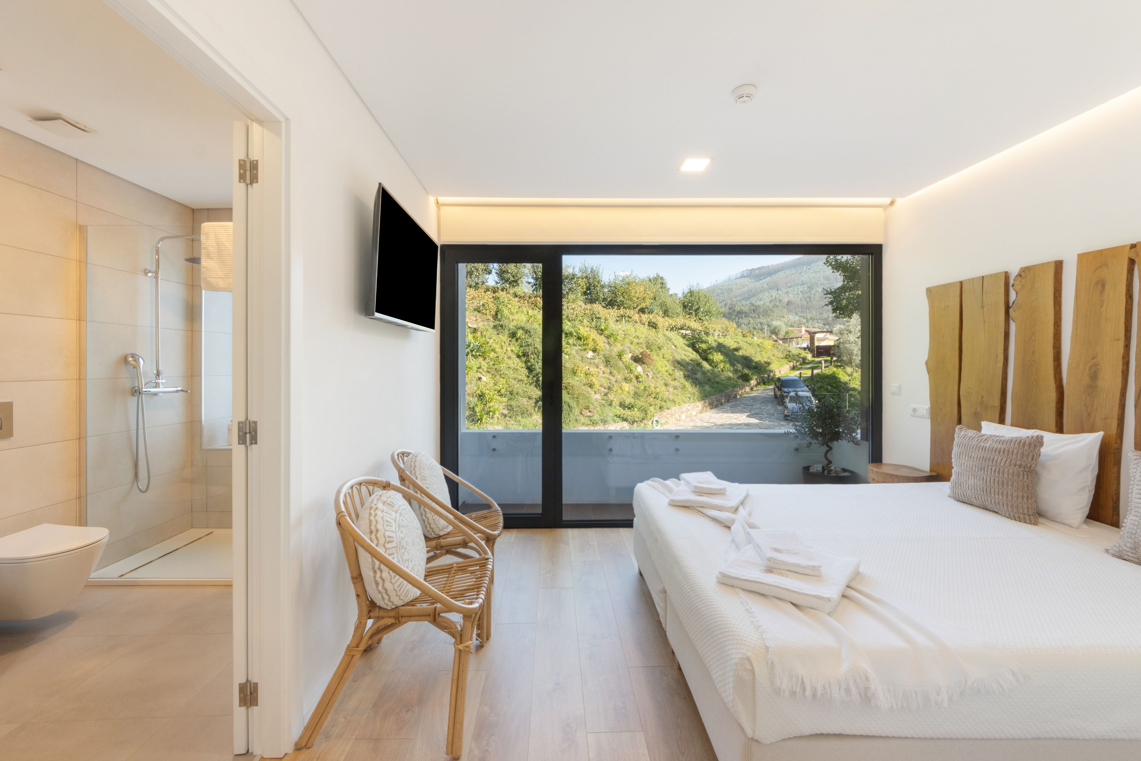 Un dormitorio moderno con una cama grande, ducha, una silla y televisor montado en la pared.