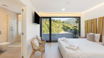 Un dormitorio moderno con una cama grande, ducha, una silla y televisor montado en la pared.