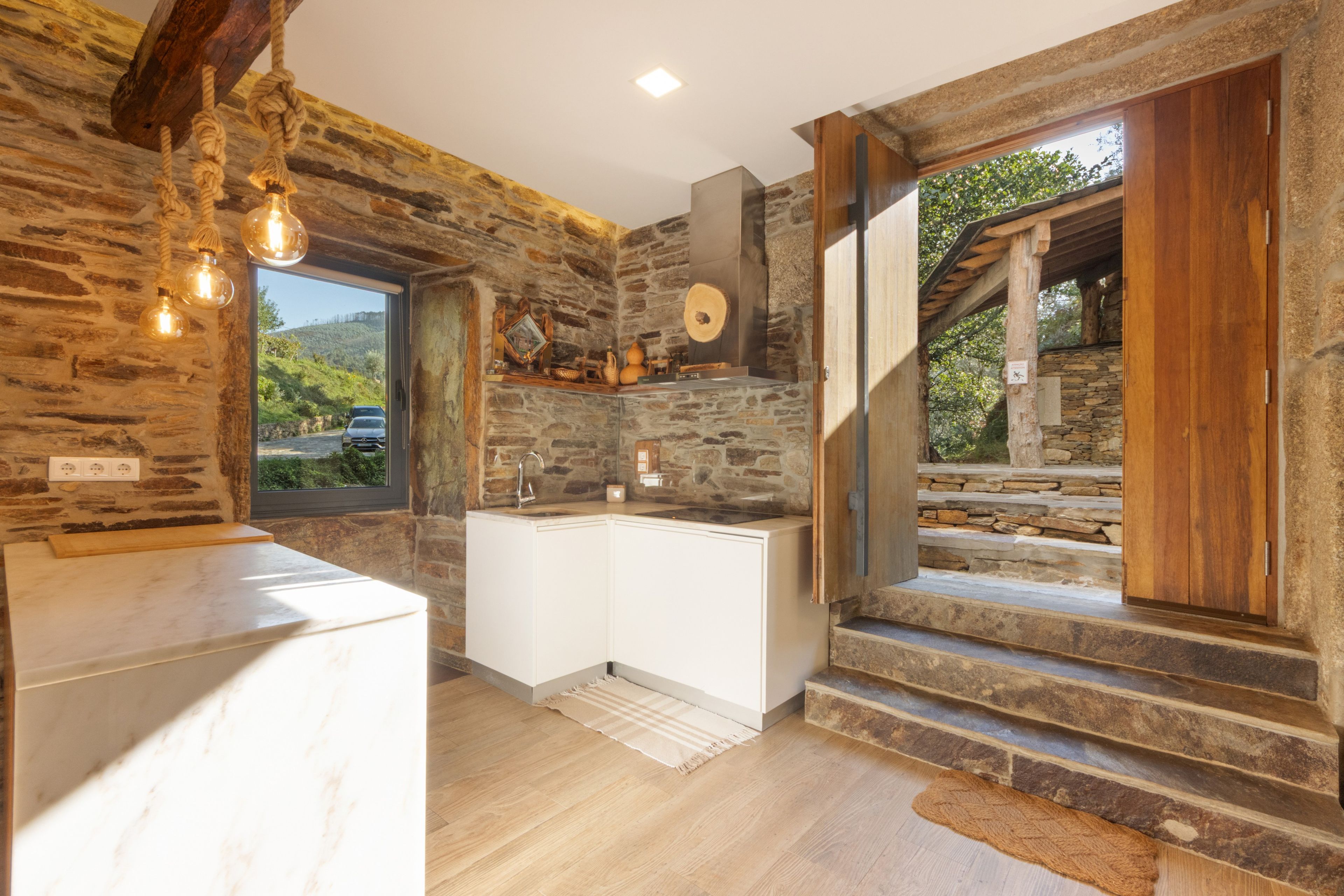 A rustic kitchen with stone walls, a wooden counter, and a view of the outdoors.