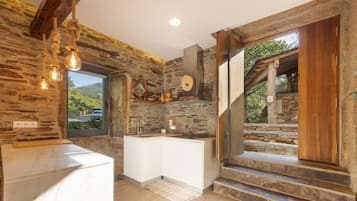 A rustic kitchen with stone walls, a wooden counter, and a view of the outdoors.