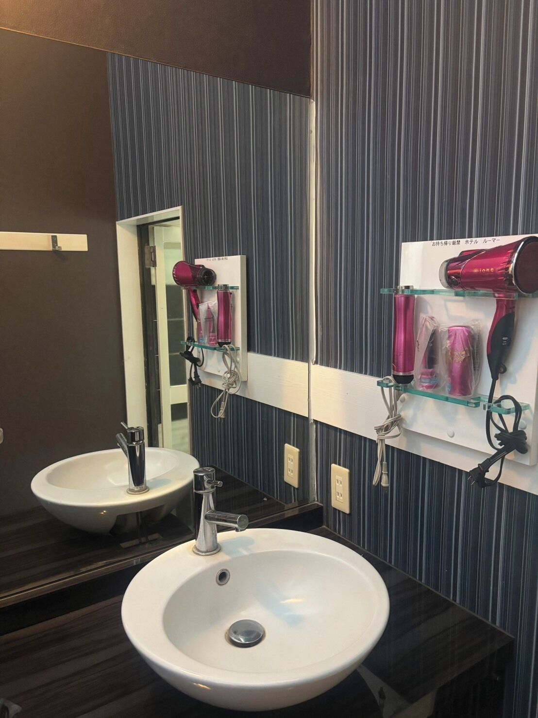 Une salle de bain avec un lavabo blanc, un miroir et un sèche-cheveux fixé au mur.