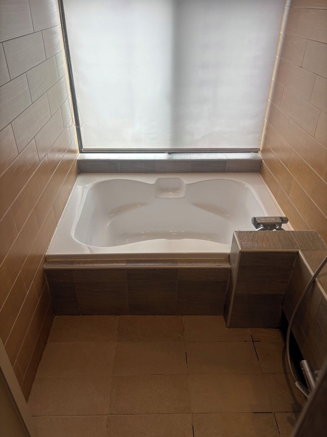 A bathroom with a bathtub, a window, and tiled walls.