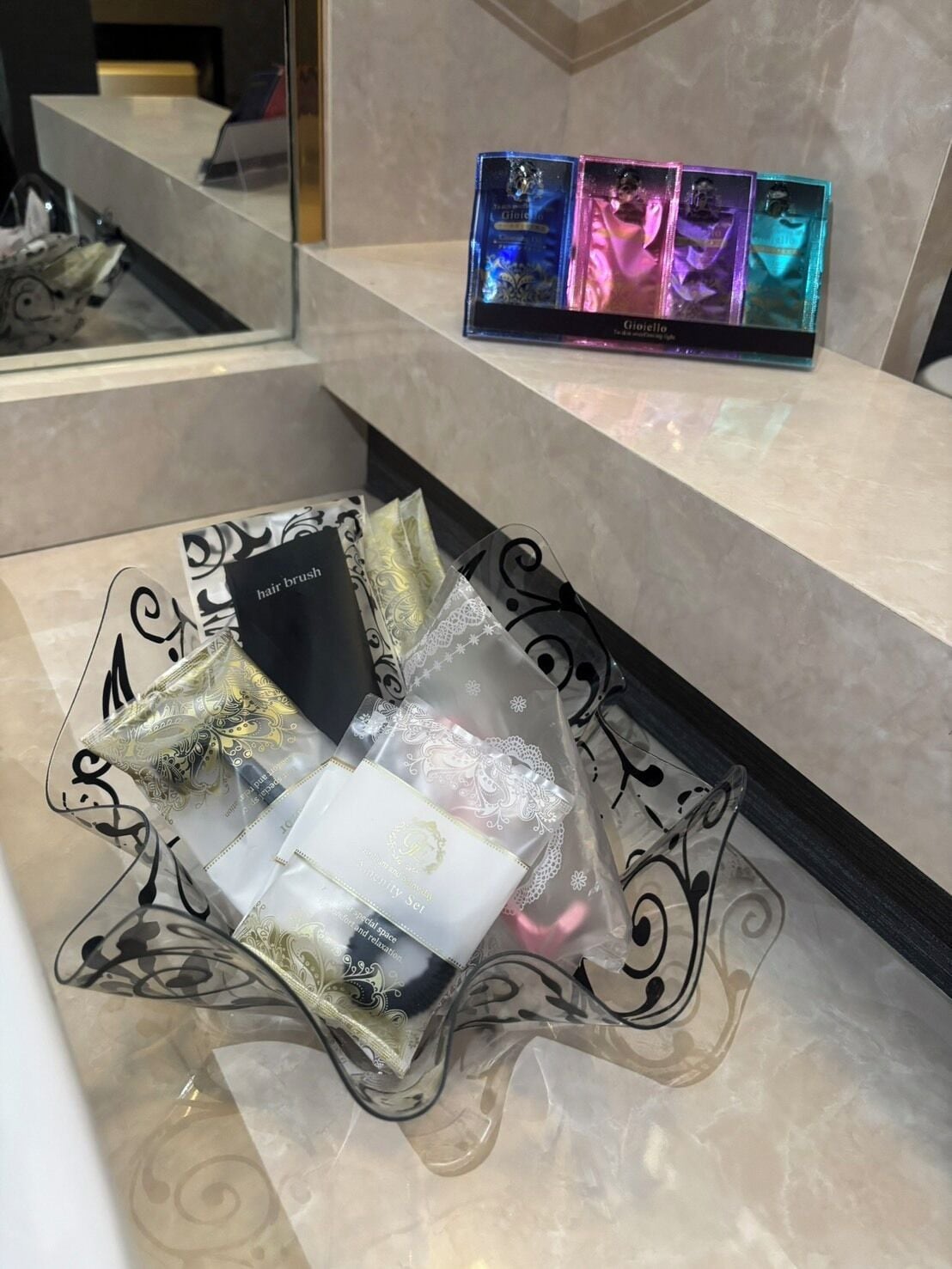 Zona de recepción de un hotel con mostrador de mármol, exhibición de cepillos de pelo y un cuenco de vidrio decorativo con artículos de aseo.