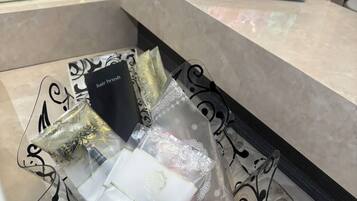 Zona de recepción de un hotel con mostrador de mármol, exhibición de cepillos de pelo y un cuenco de vidrio decorativo con artículos de aseo.