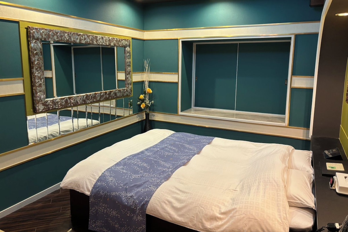 Una habitación de hotel con una cama, un espejo grande, una ventana y un florero con flores.