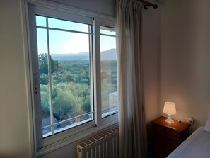 Una stanza con una grande finestra, un comodino con una lampada e un termosifone.