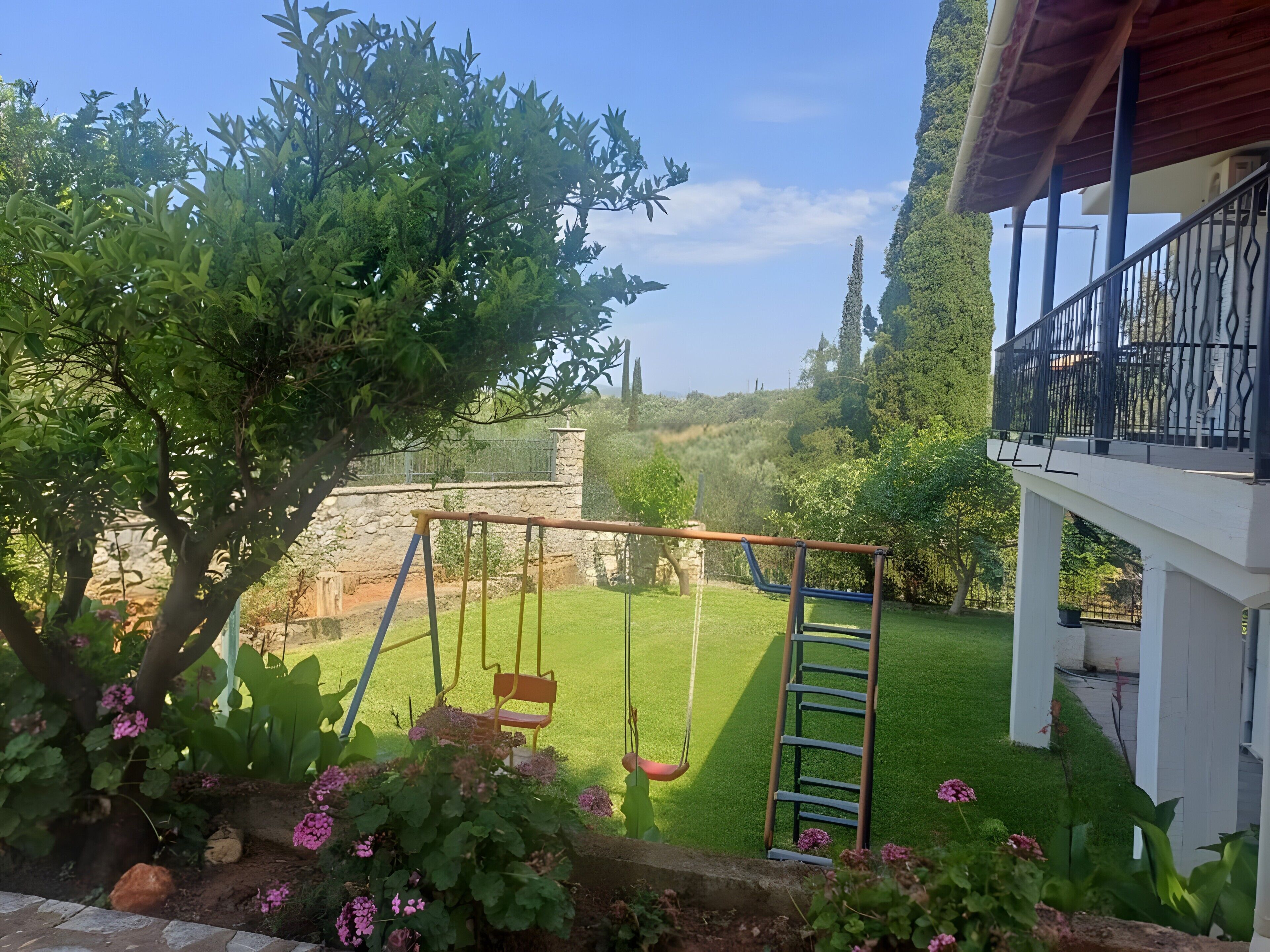 Un jardin avec une balançoire, une échelle et un bâtiment blanc doté d’un balcon.