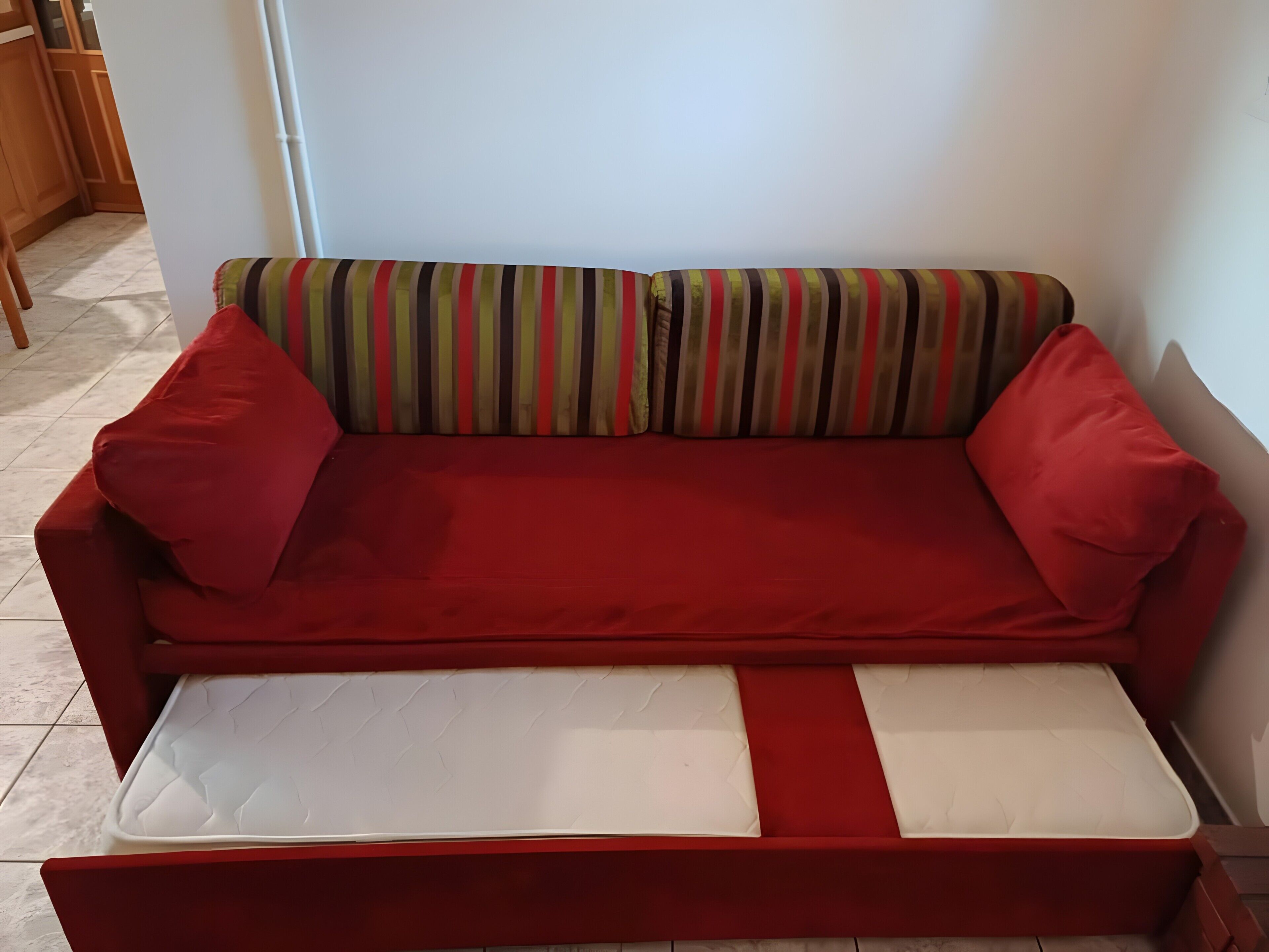 Un divano rosso con un cuscino a righe e un materasso bianco.