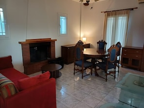 A living room with a fireplace, a dining table with chairs, a red sofa, and a glass coffee table.