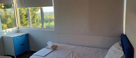 A bedroom with a bed, a desk, and a window with a view of greenery.