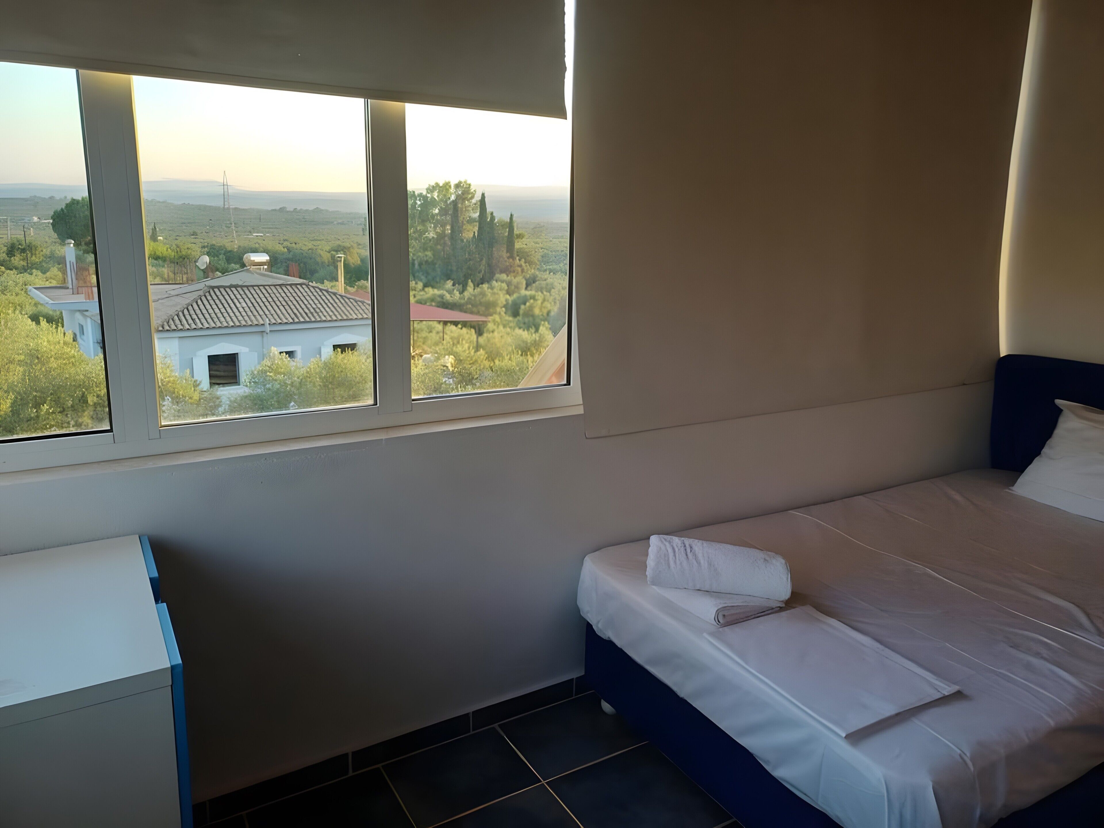 A bedroom with a single bed, a desk, and a window with a view of a landscape.