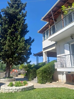 Un edificio a due piani con un balcone, un vialetto in pietra e un grande albero.
