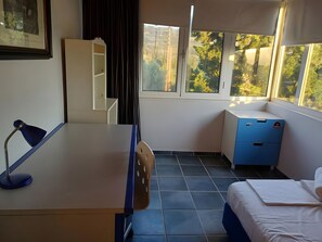 A room with a bed, a desk, a chair, a small cabinet, and a window with a view of trees.