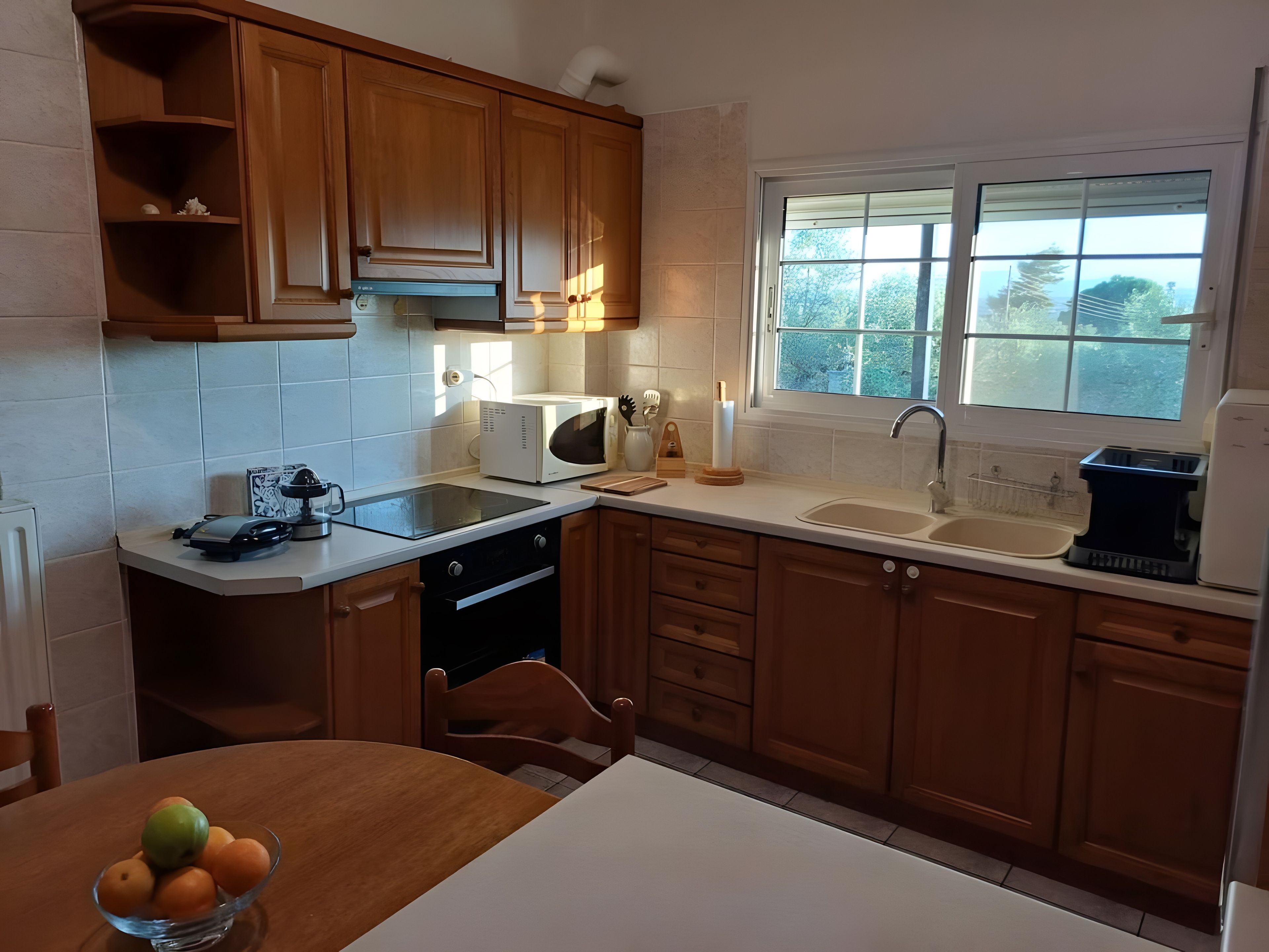 A kitchen with wooden cabinets, a white countertop, a built-in oven, a sink, and a window with a view of trees.