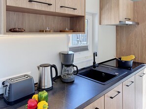 A modern kitchen with a built-in toaster, a coffee maker, a sink, and a window with blinds. - Tiny Haus Christas Oase by Interhome (Riedenburg)