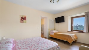 A bedroom with two beds, a window with a view, a flat-screen TV, and a radiator.