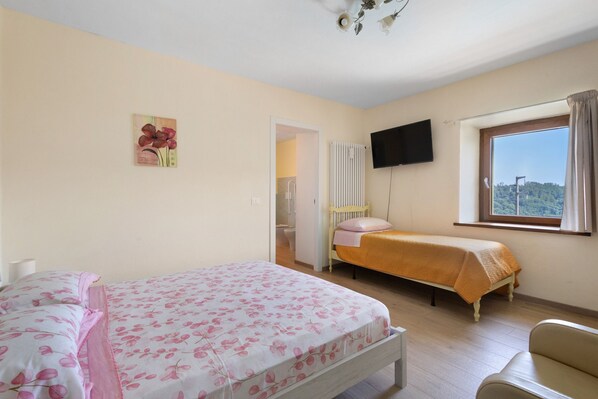 Een slaapkamer met twee bedden, een raam met uitzicht, een flatscreen televisie en een radiator.