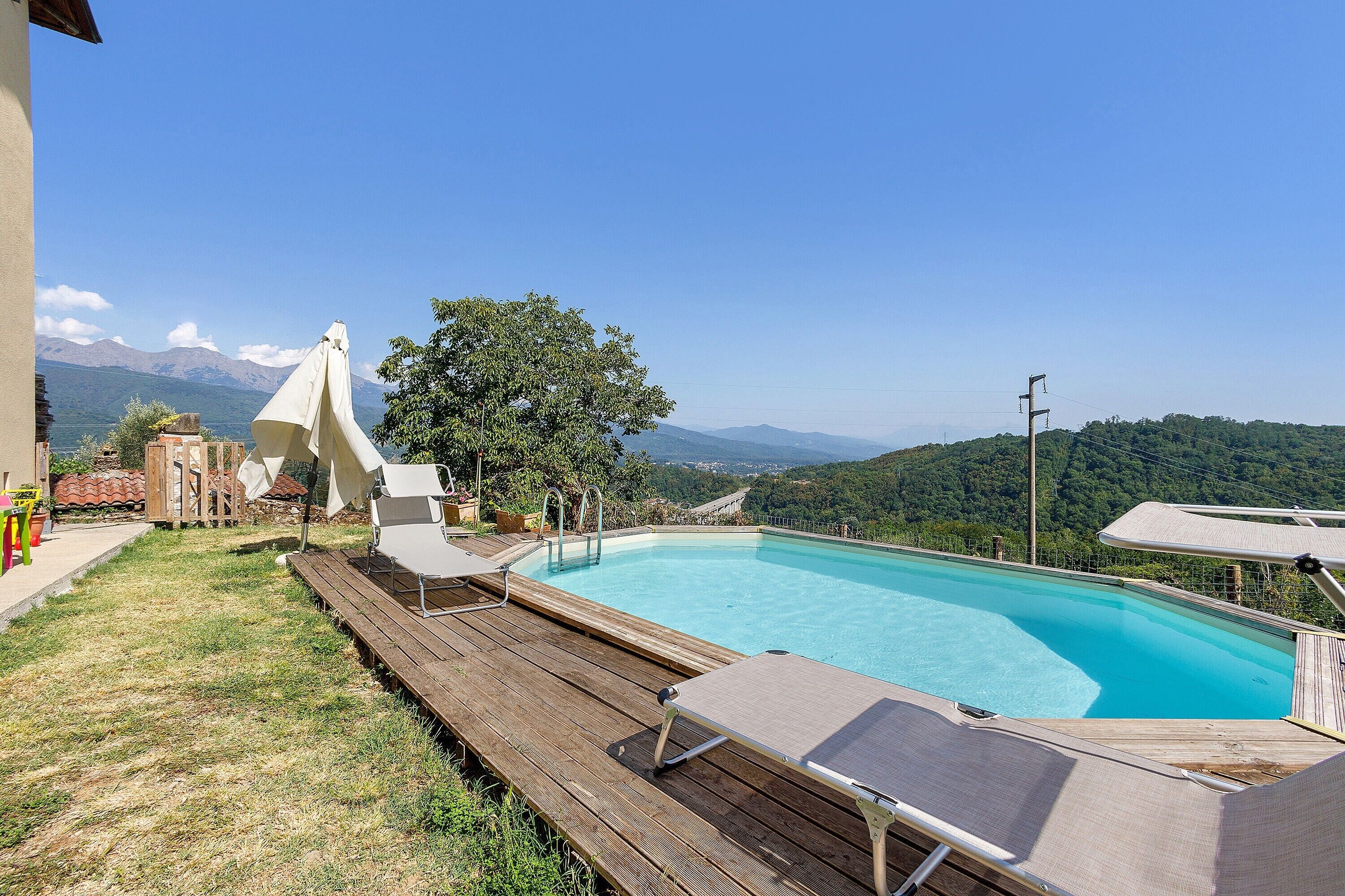 Una piscina con muelle de madera y sillones de descanso, rodeada por un paisaje montañoso.