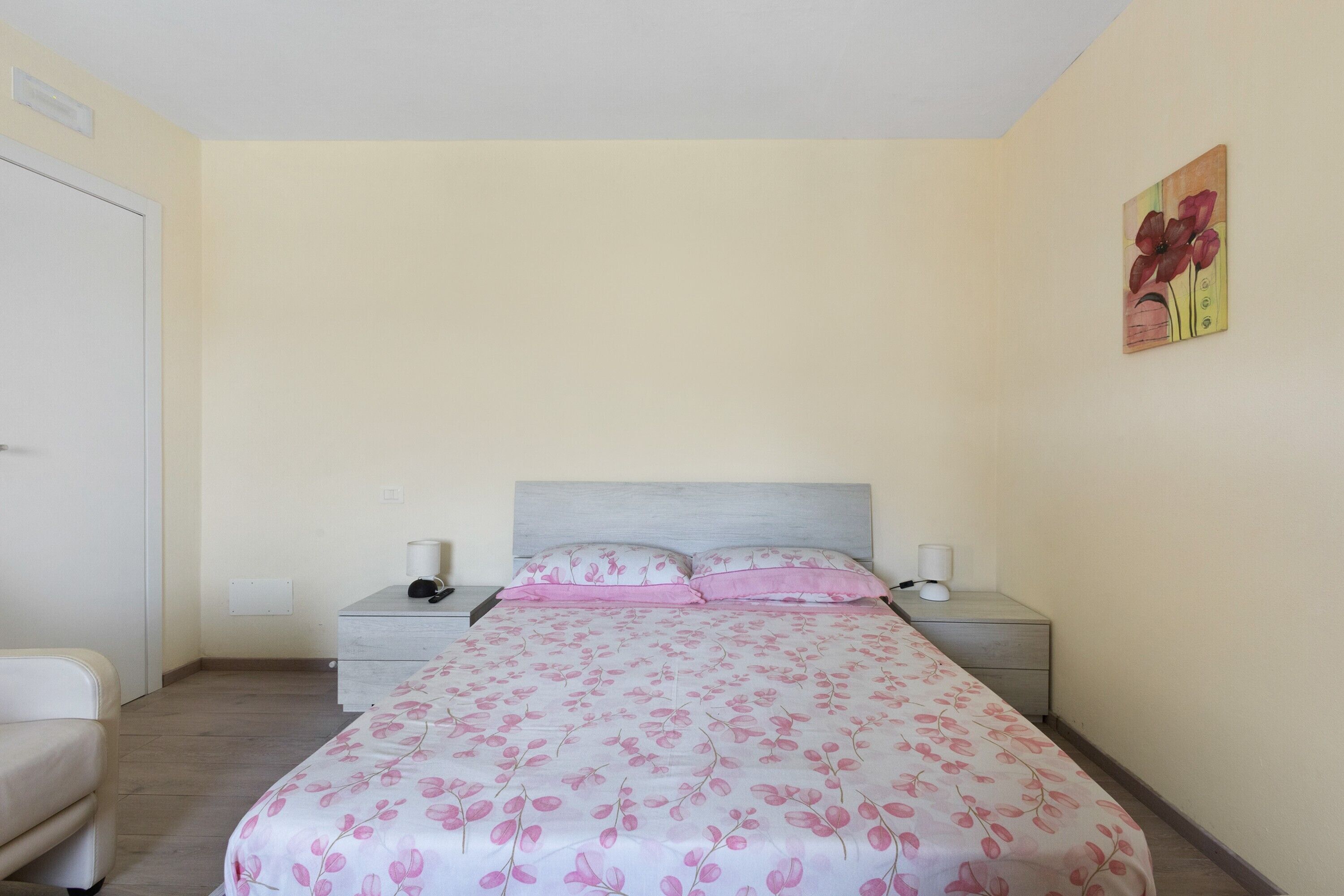 Un dormitorio con una cama, mesitas de noche, una silla y un cuadro en la pared.