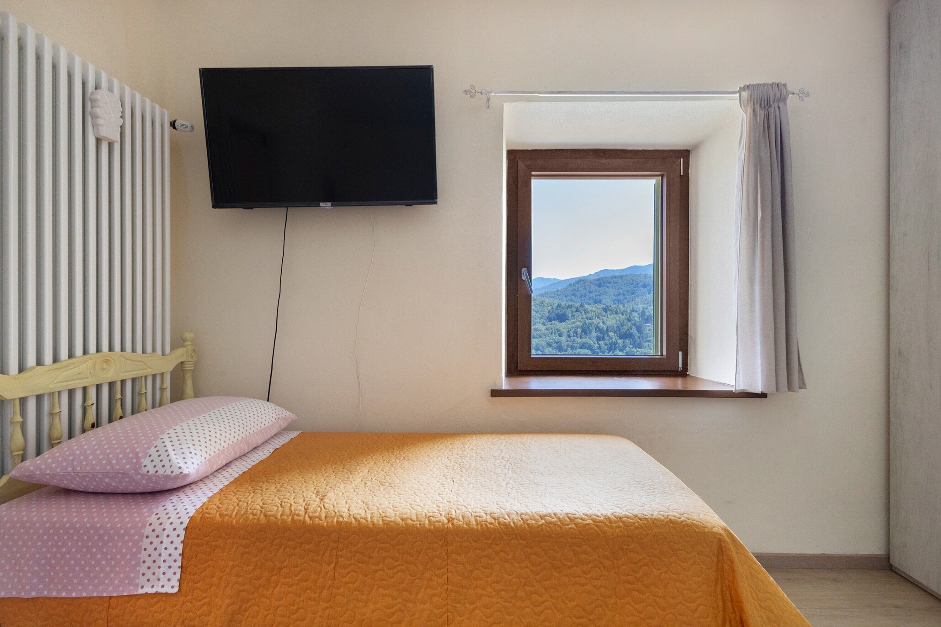 Un dormitorio con una cama, un televisor montado en la pared y una ventana con vistas a un paisaje montañoso.