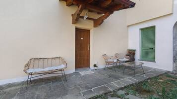 Eine terrasse mit steinbelag, Korbmöbeln, einer Holztür und einem grün verstellten Fenster.