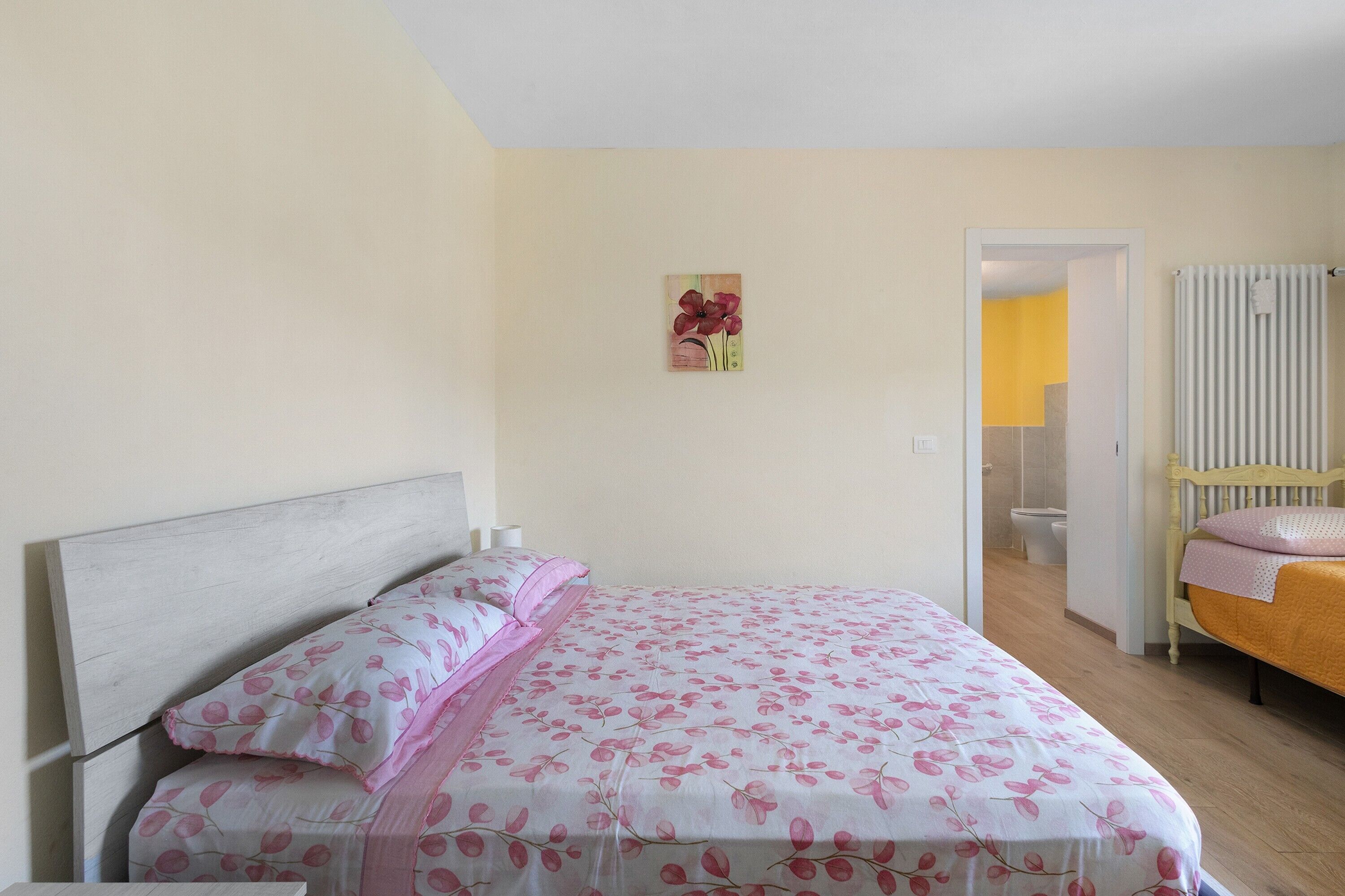 Camera da letto con un letto, un comodino, un quadro appeso al muro e un bagno visibile attraverso una porta aperta.
