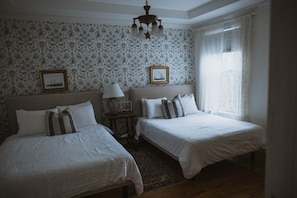 Ein Hotelzimmer mit zwei Betten, einem Nachttisch, einer Lampe, einer Uhr und einem Fenster mit Vorhängen.