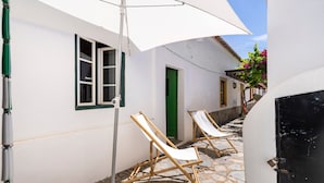 A courtyard with white walls, a green door, and two wooden lounge chairs under a white umbrella.
