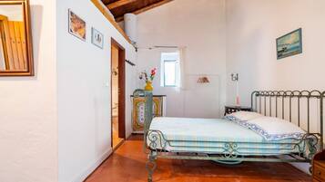 A bedroom with a metal bed frame, a wooden dresser, a small table with a lamp, and a window with a view of the outside.