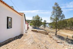 A narrow street with a white building on the left, a dirt path, and trees on the right. - Villa 'Casa Do Rio' with Private Garden, Wi-Fi and Air Conditioning (Mértola)