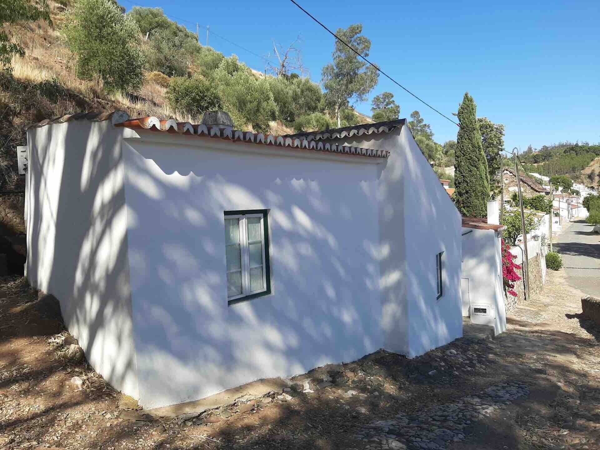 Un petit bâtiment d’un seul étage, à l’extérieur blanc et doté d’un toit en tuiles, entouré d’un paysage naturel et de végétation.