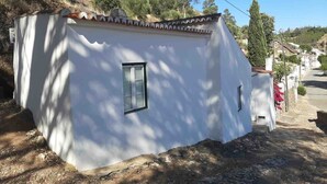 Un petit bâtiment d’un seul étage, à l’extérieur blanc et doté d’un toit en tuiles, entouré d’un paysage naturel et de végétation.