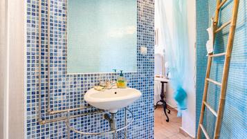Un baño con un lavamanos blanco, azulejos de mosaico azules, un espejo y una cortina de ducha.