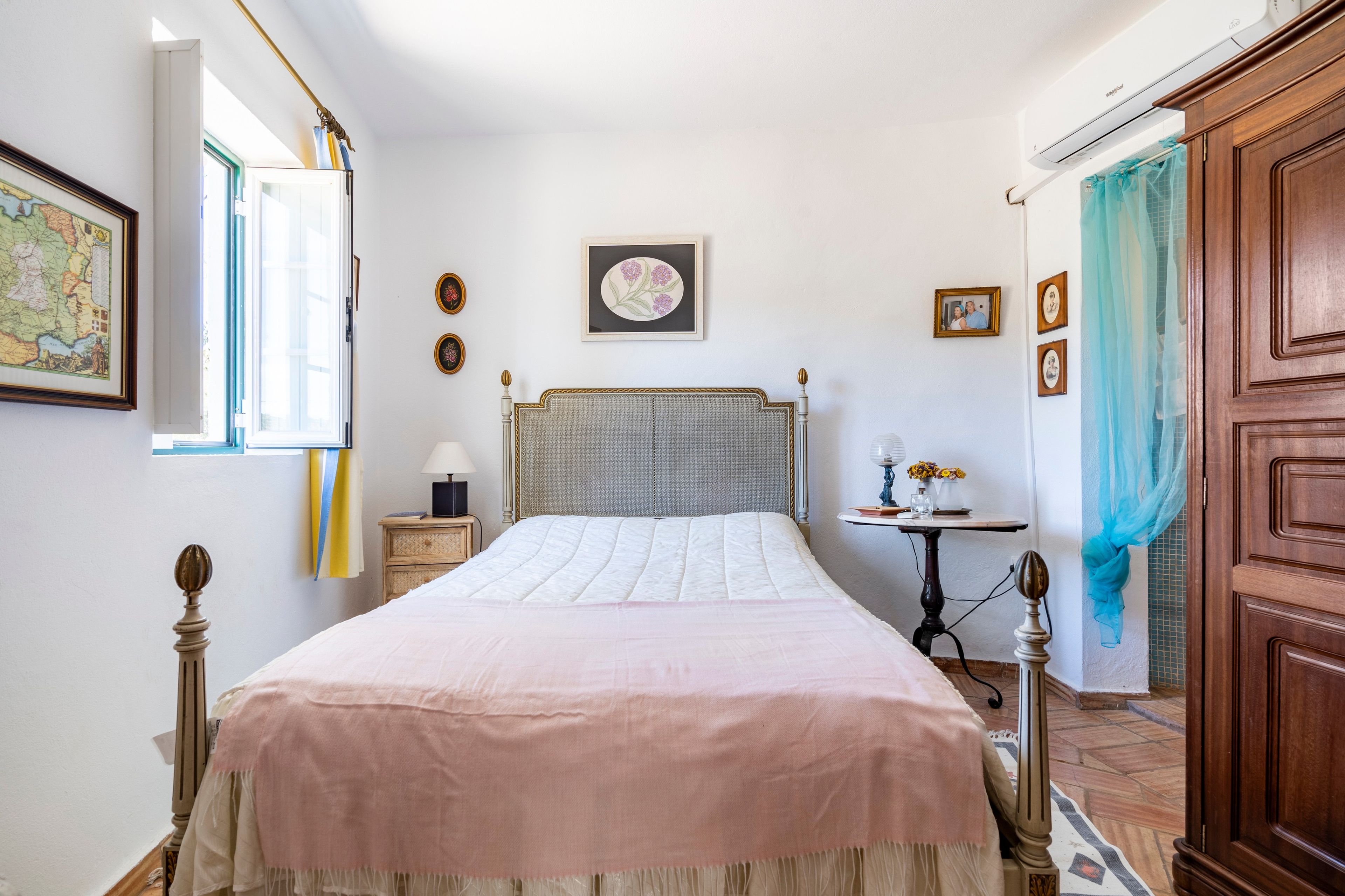 Une chambre à coucher comprenant un lit, une table de chevet, une commode, une fenêtre avec des rideaux et un climatiseur fixé au mur.