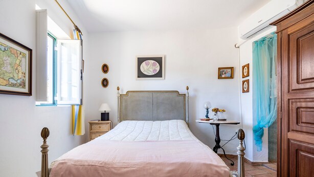 A bedroom with a bed, a nightstand, a dresser, a window with curtains, and a wall-mounted air conditioner.