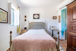 Un dormitorio con cama, mesita de noche, cómoda, ventana con cortinas y aire acondicionado instalado en la pared.