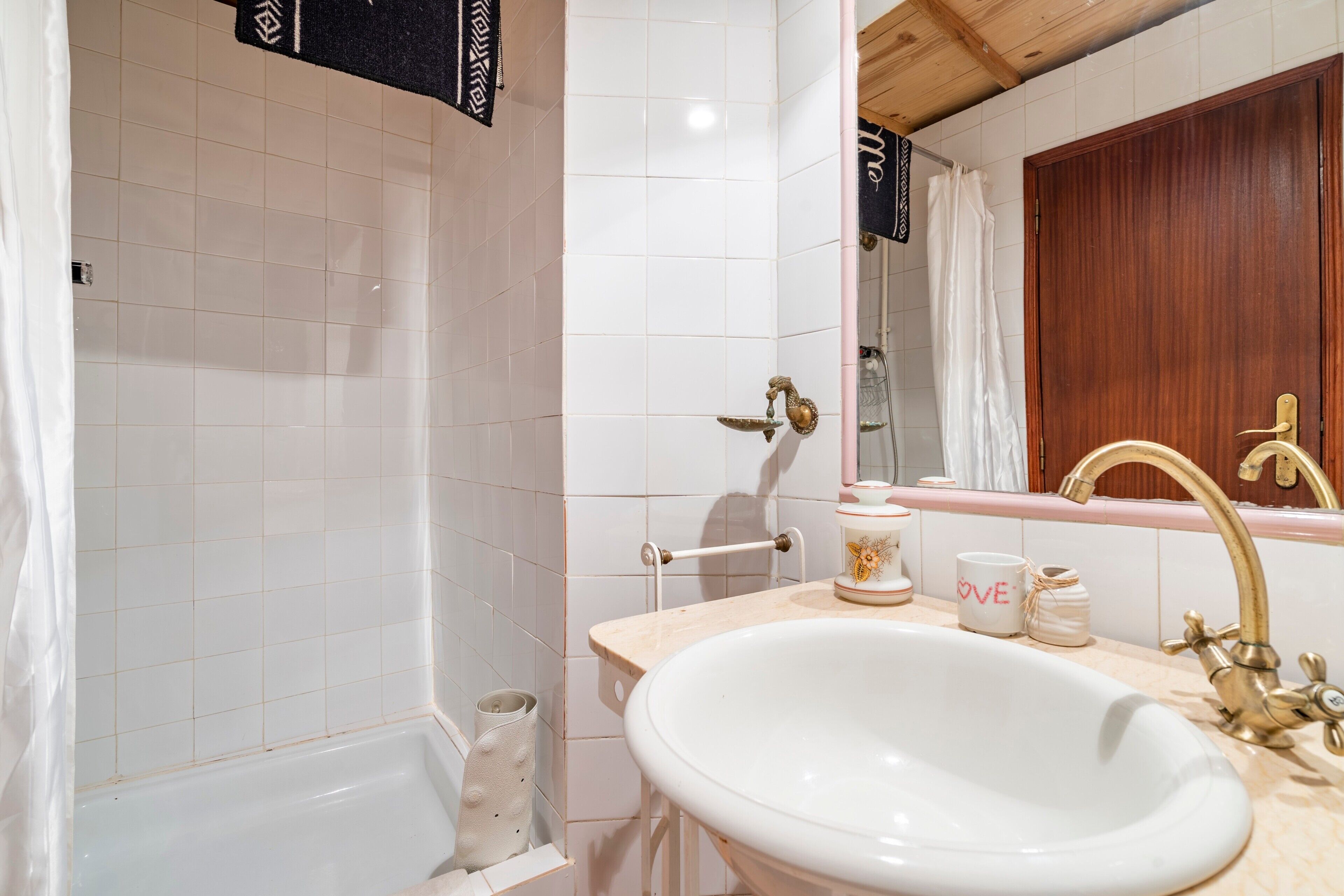 Une salle de bain avec une baignoire blanche, un lavabo avec un robinet doré et un meuble en bois.