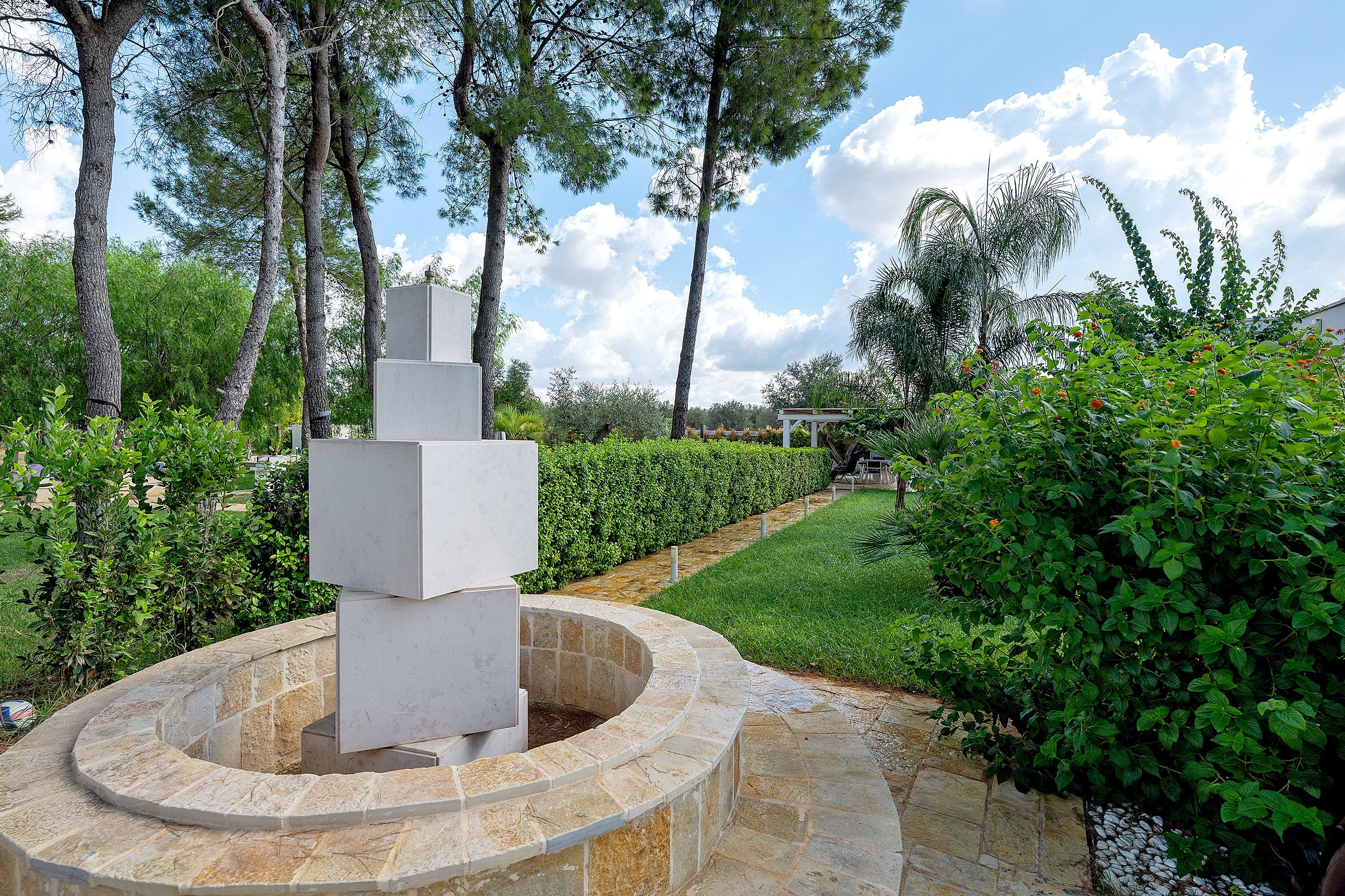 A landscaped garden with a central stone fountain, surrounded by neatly trimmed hedges and trees.