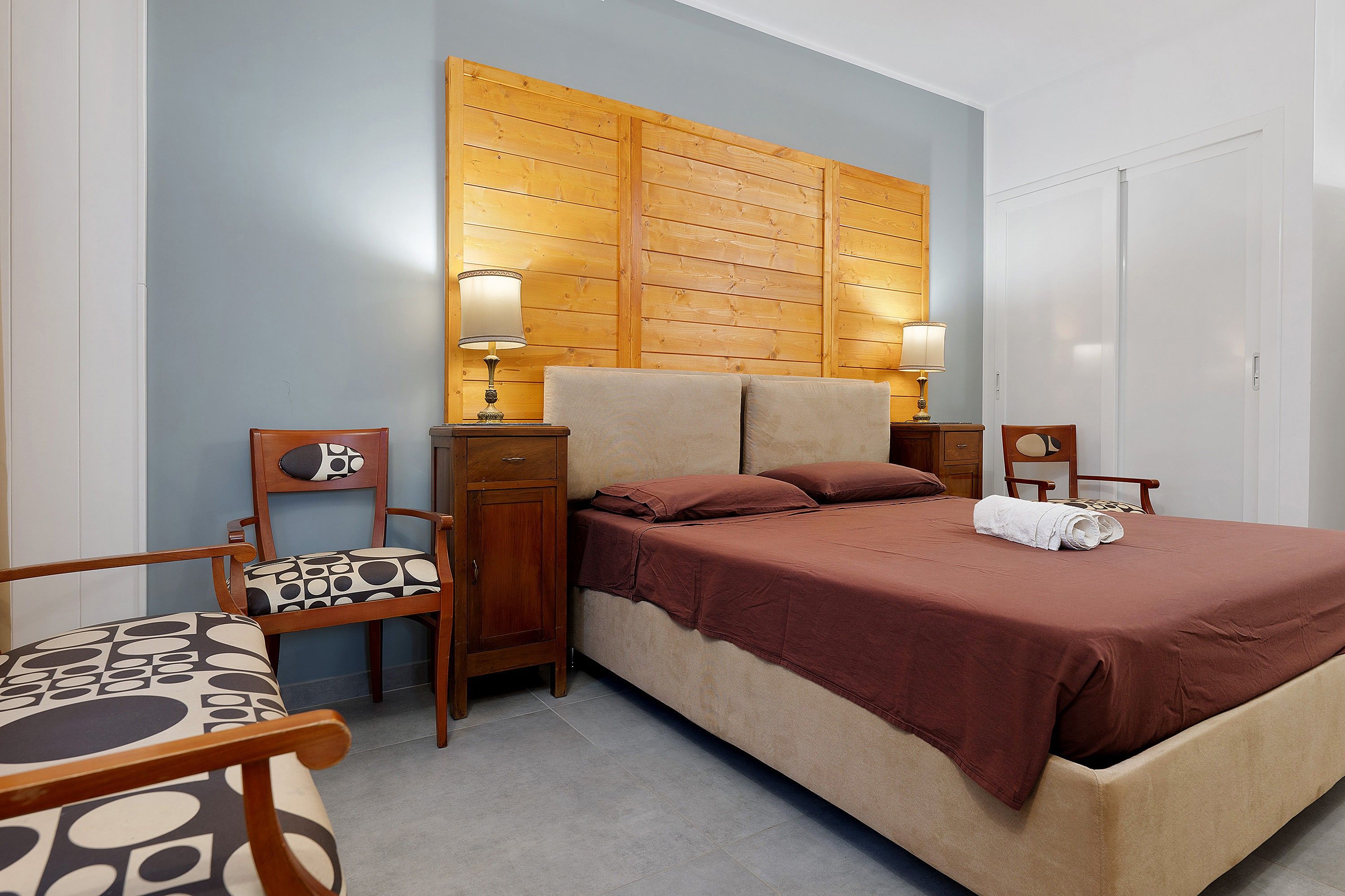 A hotel room with a bed, two bedside tables, a chair, and a wardrobe.