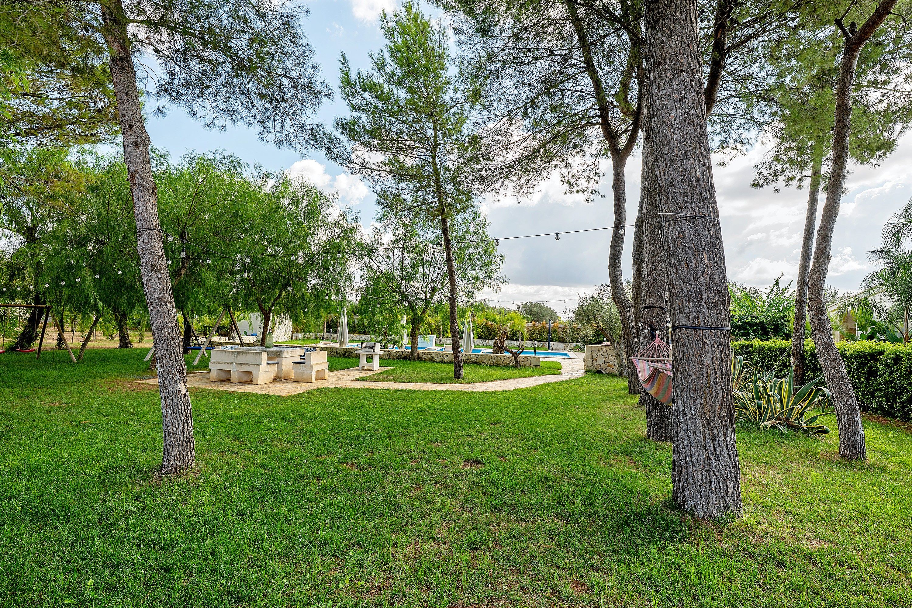 A well-maintained outdoor area with a swimming pool, seating arrangements, and a grassy lawn surrounded by trees.