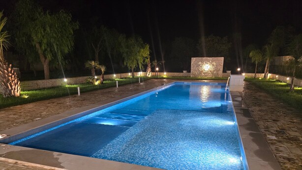 En rektangulär swimmingpool med en kant av kakel, omgiven av en stenkant och en låg stenmur.