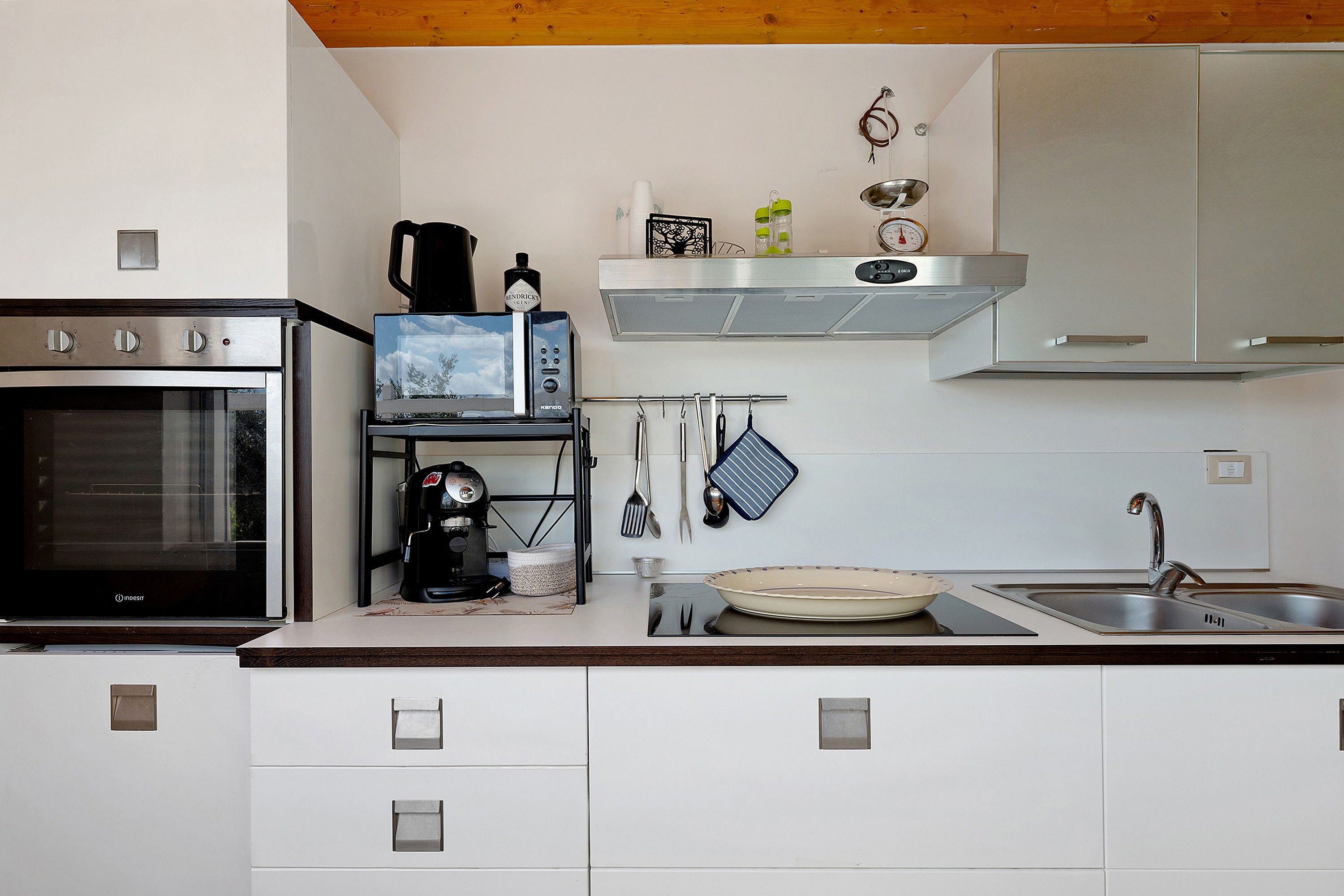 A kitchen with a built-in oven, a coffee machine, a kettle, and a microwave.