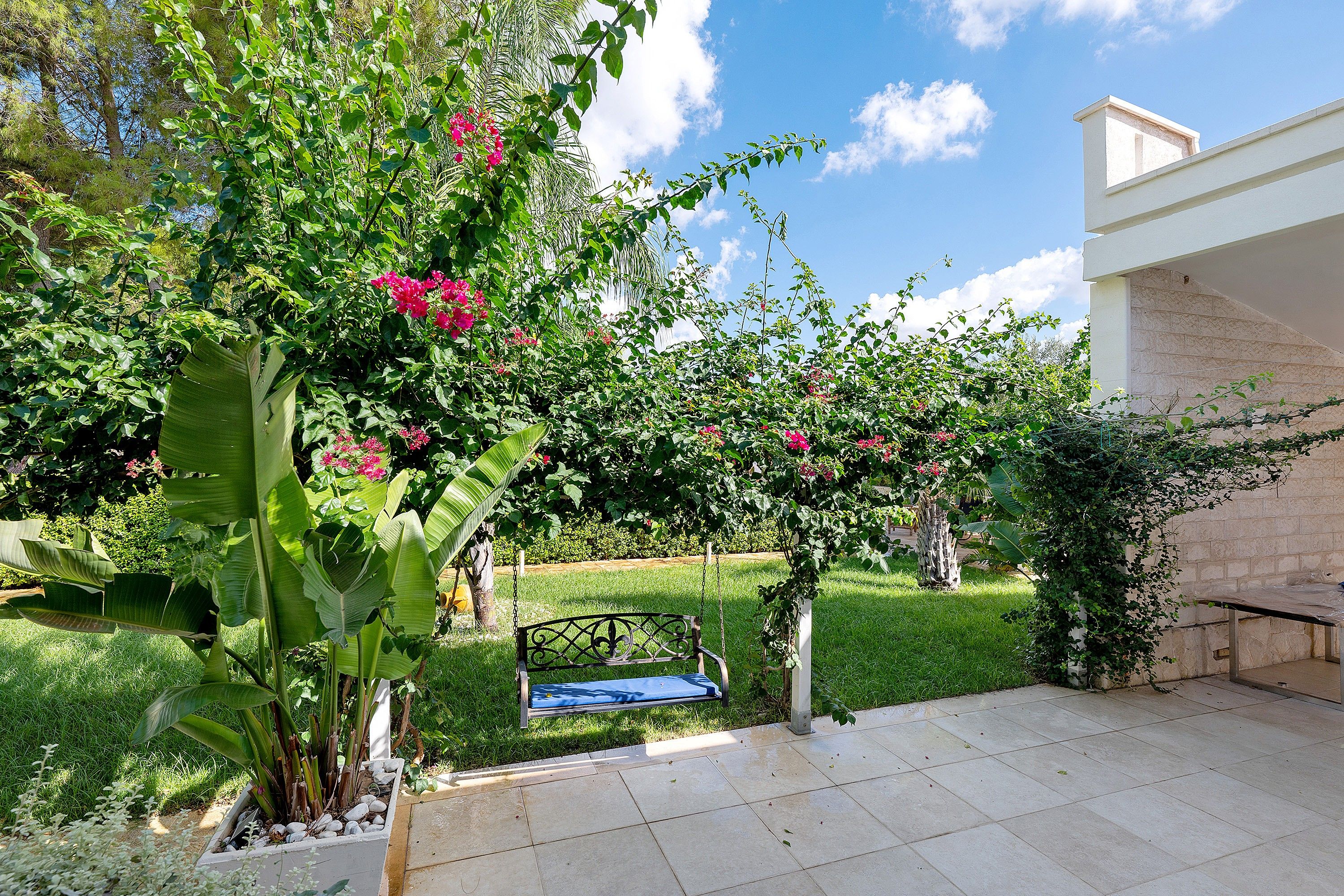 Un giardino con una panchina, un muro bianco e un cielo sereno.