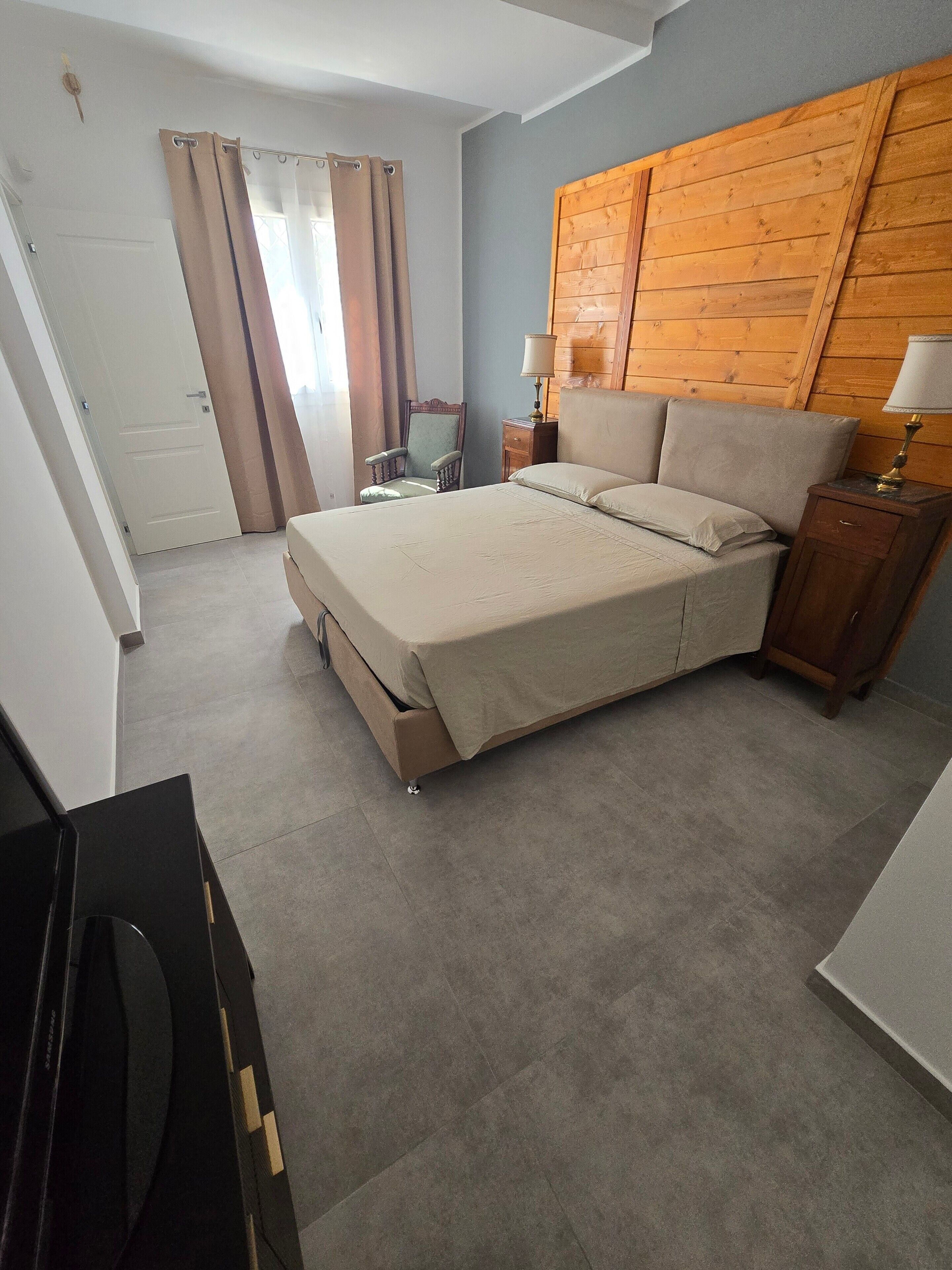 Une chambre à coucher avec un lit, une tête de lit en bois, une table de chevet avec une lampe, une chaise et une porte.