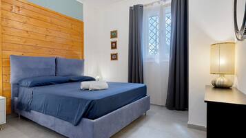 Une chambre à coucher avec une tête de lit en bois, un lit avec une literie bleue, une table de chevet avec une lampe et une fenêtre avec des rideaux.