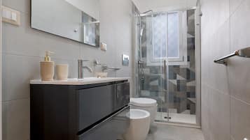 Un bagno moderno con un mobile lavabo scuro, un water e un box doccia in vetro.