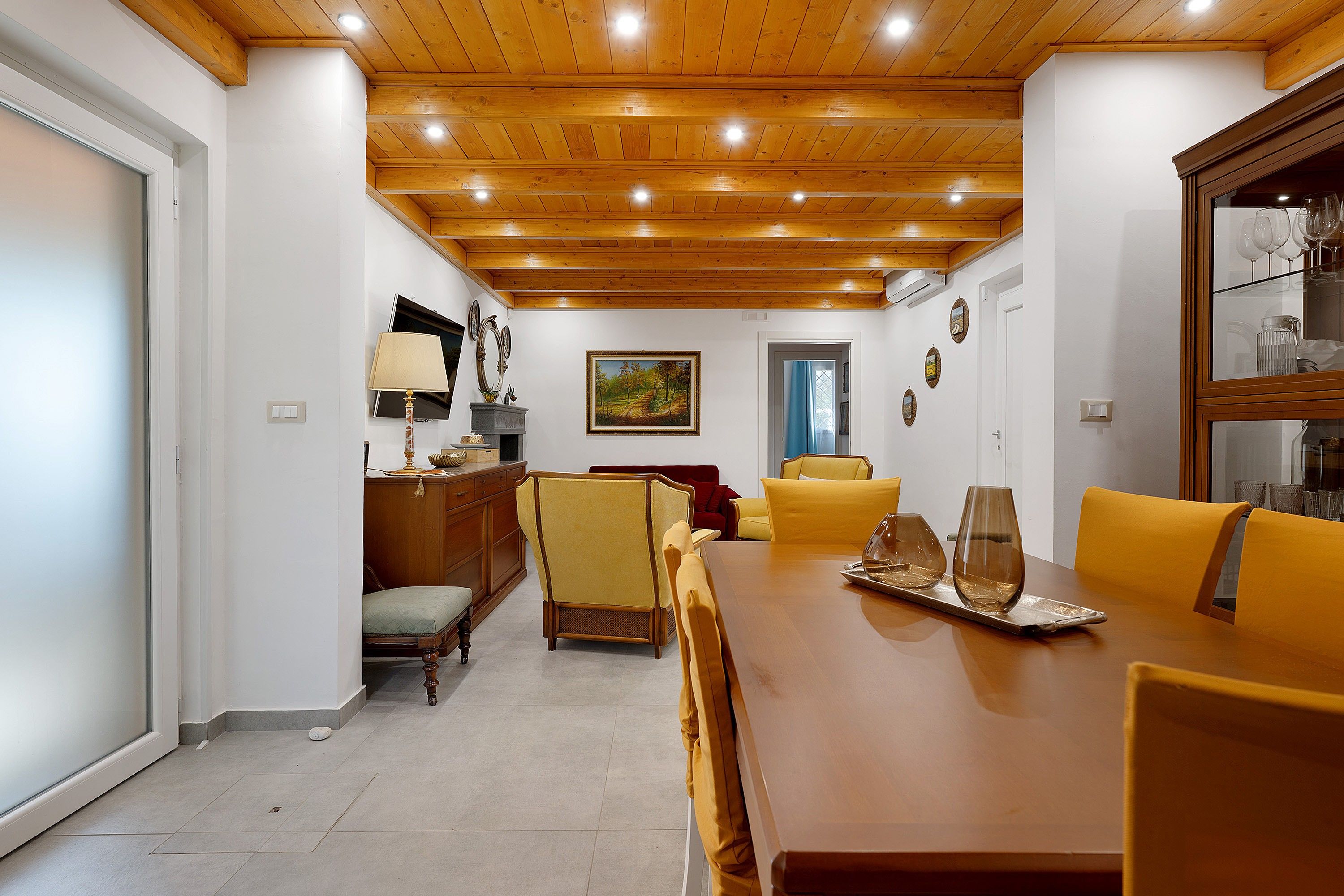Un área de comedor con una mesa de madera, sillas amarillas y una mesa con cubierta de vidrio.